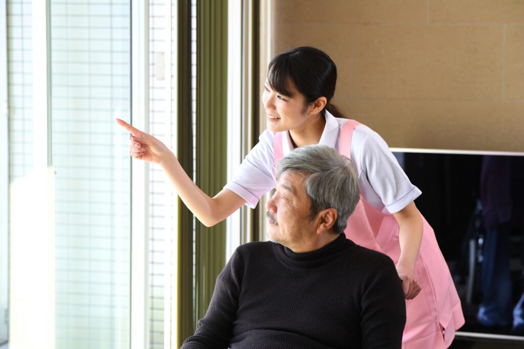 室内で車椅子を押す若い女性とシニア男性